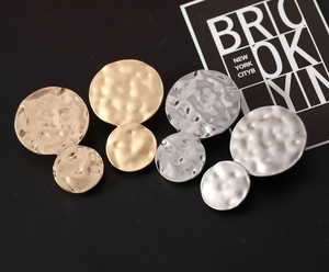 Detailed macro view of gold and silver textured double circle earrings set on black card