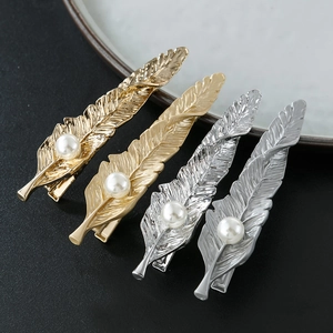 Detailed macro view of four alloy feather hair clips with pearls on black texture