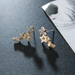 Detail of gold climber earrings with star shapes and sparkling rhinestones on grey background