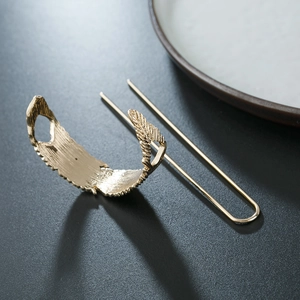 Detail of gold alloy leaf hair slide and U-shaped pin on a dark textured surface