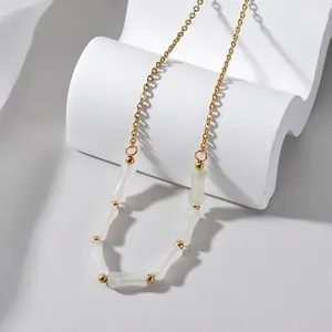 Elegante collana con perline in bambù dorato su supporto geometrico bianco puro