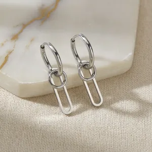 Polished silver geometric hoop earrings with oval pendants on a stone display base