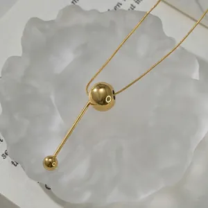 Detail of a golden snake chain necklace with a round bead pendant on a glass tray