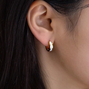 Minimalist gold hoop earrings with white enamel inlay shown on a model's ear