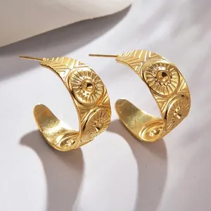 Close-up of golden C-shaped earrings with sunburst relief and bohemian texture detail