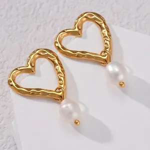 Close-up of hammered gold heart earrings with white teardrop pearl drops