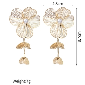 Detailed view of hollow gold flower earrings with pearls and long metal leaf tassels