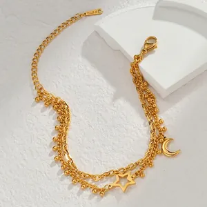 Macro detail of 18K gold-plated stainless steel star and moon charms on double-layer chain