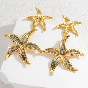 Detail von goldenen Seestern-Ohrringen mit Abalone-Muschel auf strukturiertem weißem Stein