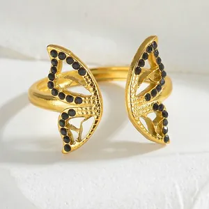Polished gold butterfly open ring with black crystals on white marble background