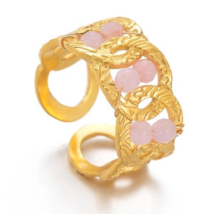 Detail of gold geometric interlocking ring with pink bead accents and engraved texture