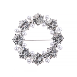Silver wreath brooch with white pearls and sparkling red rhinestones on a white background