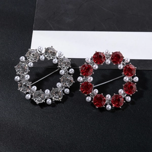 Detailed view of two circular brooches with red crystals, pearls and silver finish