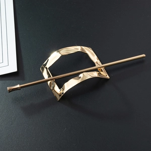 Detail shot of a hollow geometric gold hair pin with a polished metallic finish on black