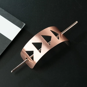 Detailed close-up of rose gold hollowed metal hair pin with brushed triangle patterns