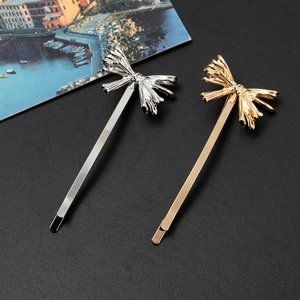 Détail de barrettes à nœud en métal doré et argenté sur fond noir texturé