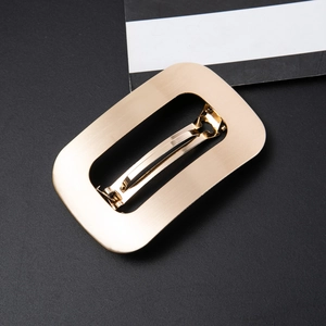 Detail of golden rectangle hair clip showing brushed metal texture and spring fastener