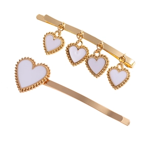 Close-up of golden alloy heart hair clips set with white enamel and beaded edge detail