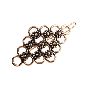 Detail of vintage bronze hair clip featuring hollow metal rings and daisy flower patterns