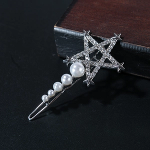 Close-up of star hair clip with crystals and five gradient white pearls on dark wood
