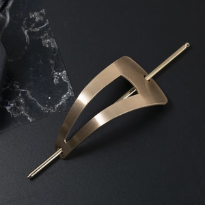 Detail view of matte gold triangle hair stick with brushed metal texture on black marble