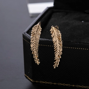 Macro view of gold leaf feather earrings with fine carved texture on a black gift box