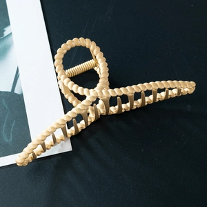 Matte champagne gold twisted hair claw clip with green accents in a minimalist style