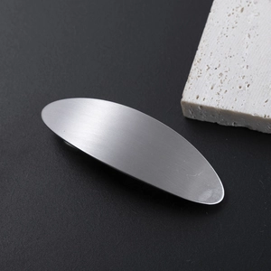 Close-up of small silver brushed metal oval hair clip on black stone background