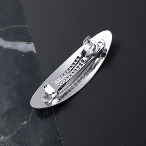 Minimalist silver oval metal hair clip with polished brushed finish on marble background