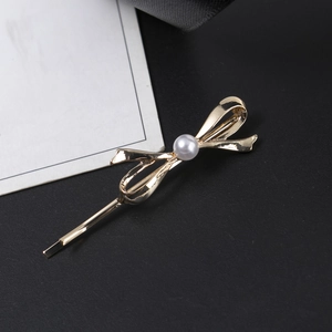 Détail d'une barrette nœud dorée ornée d'une perle sur un fond en soie noire élégante