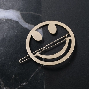 Barrette à cheveux minimaliste dorée mate avec visage souriant sur fond en marbre noir
