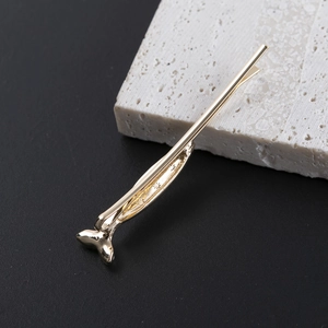 Elegant gold fish tail hairpin made of polished metal on a minimalist stone background