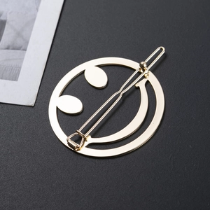 Pince à cheveux dorée minimaliste motif smiley sur une surface noire texturée élégante