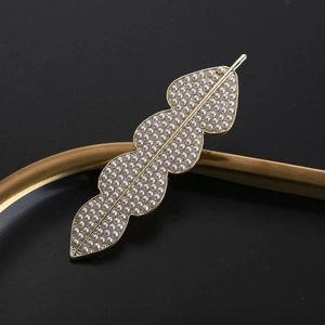 Eleganter goldener Haarclip in Blattform mit Perlen auf einem Metalltablett