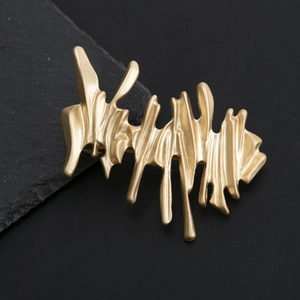 Artistic golden irregular metallic hair clip with elegant matte finish on dark stone