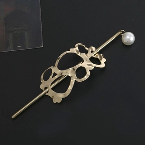 Close-up of golden hollow metal hair pin with a white pearl on a dark surface