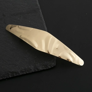 Close-up of golden spindle hair clip featuring an artistic hammered metal texture surface