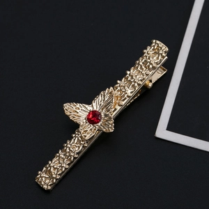 Close-up of golden vintage hair clip featuring embossed floral texture and a red rhinestone