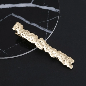 Golden alloy hair clip with hammer texture and wavy edges on black marble background