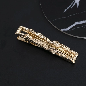 Macro detail of wave textured golden alloy duckbill hair clip on a black background
