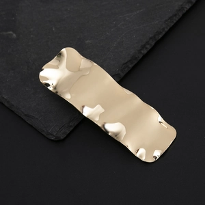 Detail of a wavy irregular gold alloy duckbill hair clip with a polished mirror finish