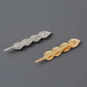 Minimalist metallic leaf hair clips in gold and silver finishes on a grey background