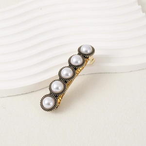 Elegant vintage hair clip with five white pearls and gold metal base on a cream surface