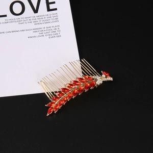 Detailed close-up of golden leaf hair comb with red rhinestones on black background