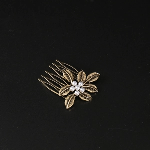 Macro detail of bronze metal leaf hair comb with six white pearls on black texture