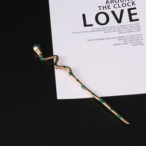 Minimalist gold-plated snake hair pin with green enamel accents on a designer card