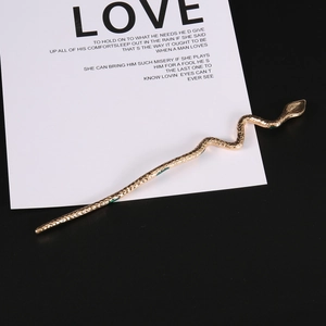 Golden snake-shaped metal hair pin with textured scales on a black and white background