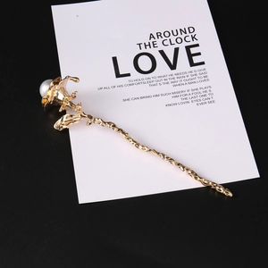 Detailed view of a gold rose hair pin with a white pearl and wavy metallic texture