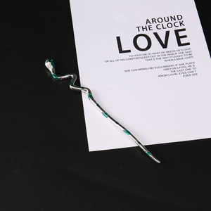 Silver metal snake hair pin with green enamel details on a minimalist poetic background