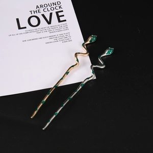 Macro shot of silver and gold snake hairpins with green enamel eyes on prop card
